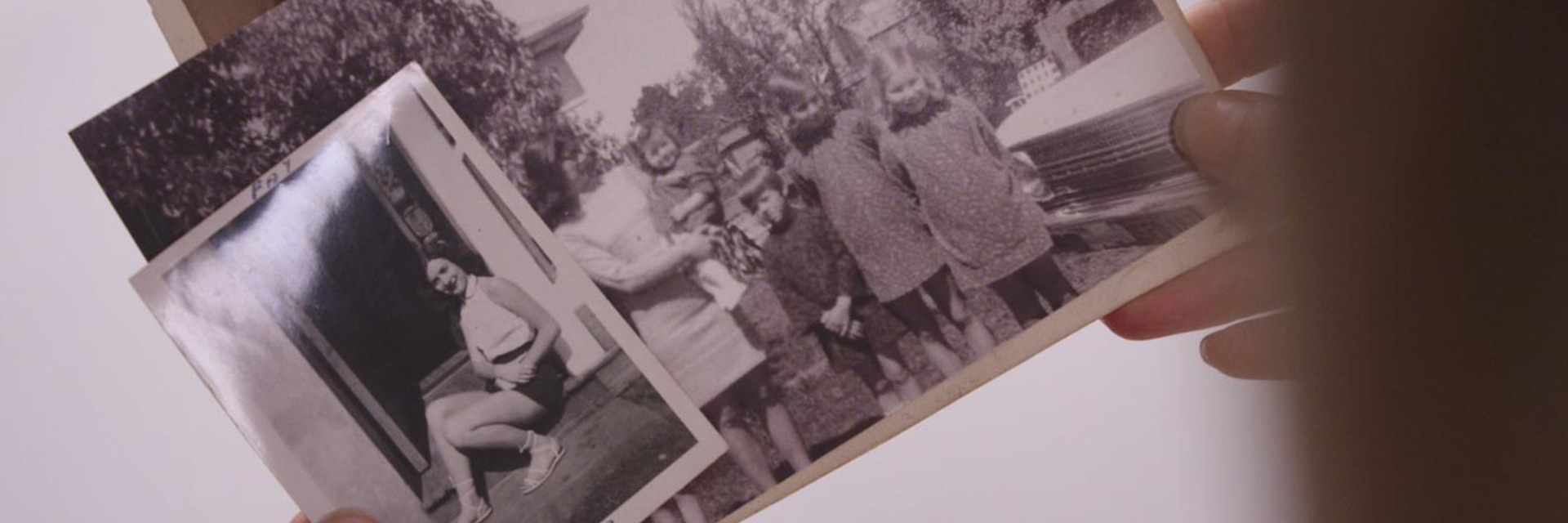 Hands hold a series of old photographs of a young woman in a doorway and a young mum with four children.