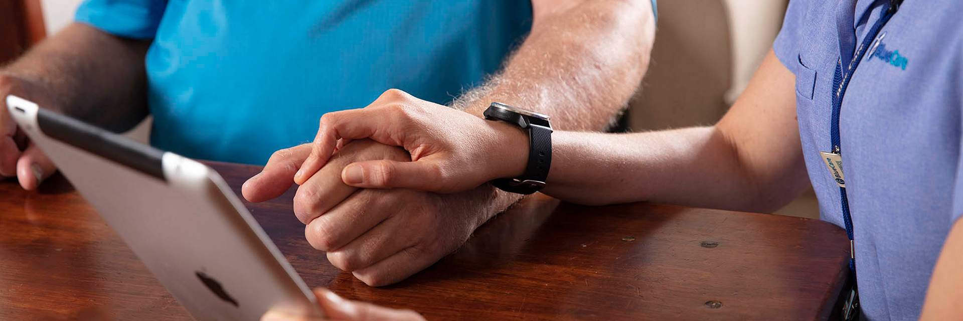 A close up photos of a Blue Care employee holding the hand of an older man while viewing a tablet