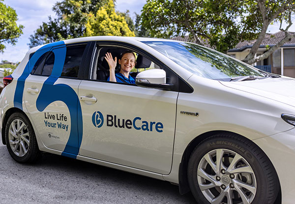 Blue Care employee in car smiling and waving at camera