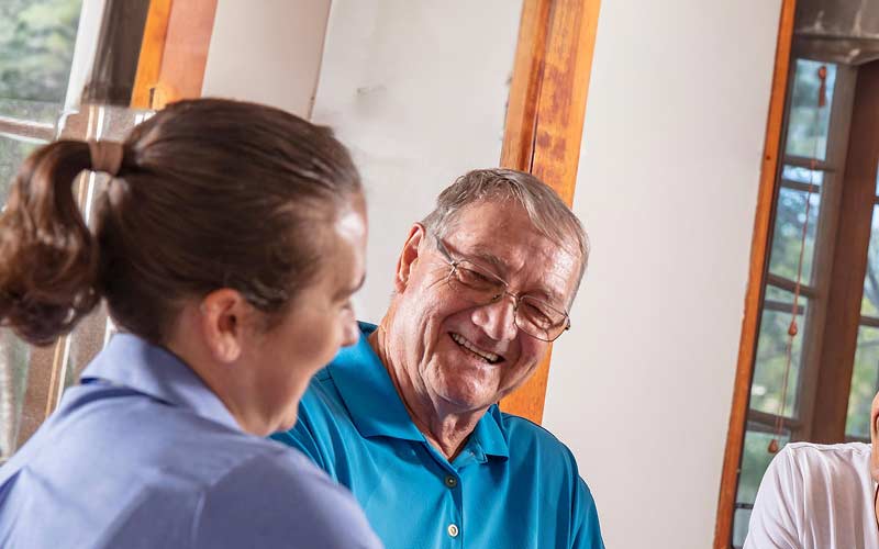 Elderly father and son in living room smiling at Blue Care worker