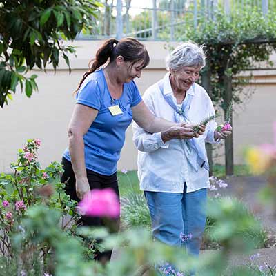 A Blue Care employee supports an older lading living with dementia to work in her garden.