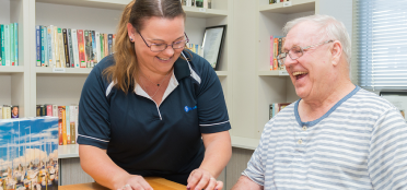 A smiling and laughing older gentlemen enjoying the company of a Blue Care employee while doing a puzzle