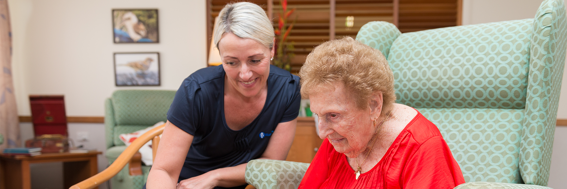 An older lady in a red shirt enjoys a puzzle with a woman who works at Blue Care Caloundra Aged Care Facility.