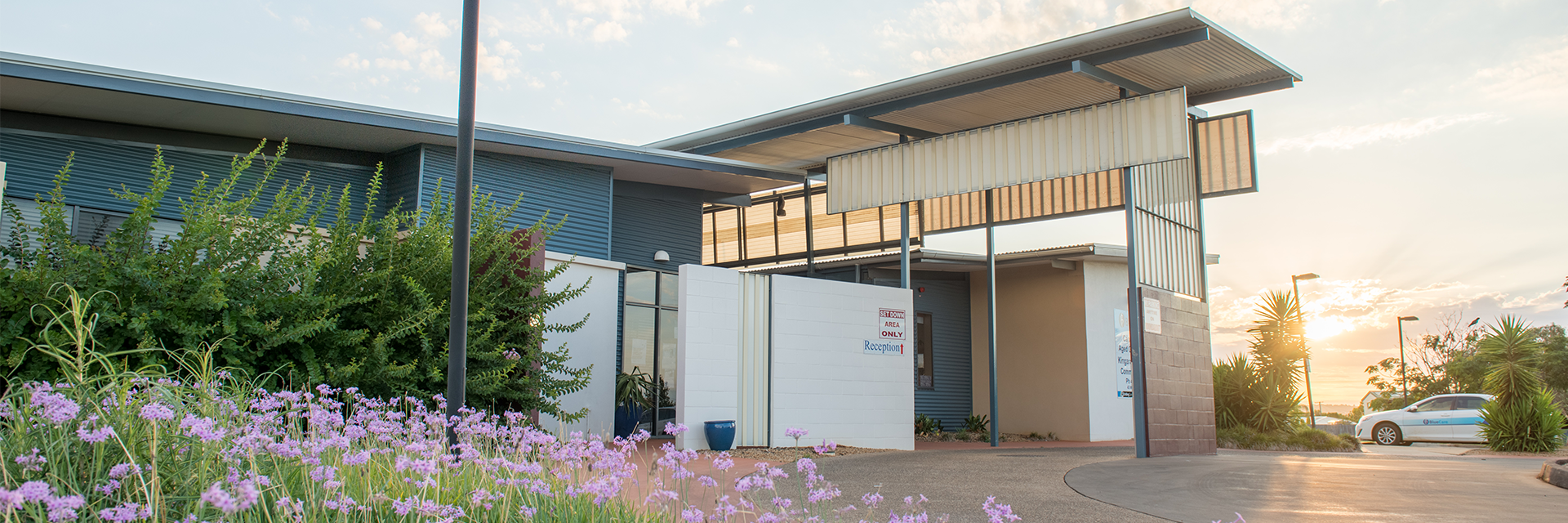 A bed of purple flowers graces the entrance to Blue Care Kingaroy Canowindra Aged Care Facility as the sun sets in the background.