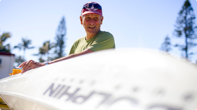 Retiree gentleman cleaning his surf ski with palm trees in the background