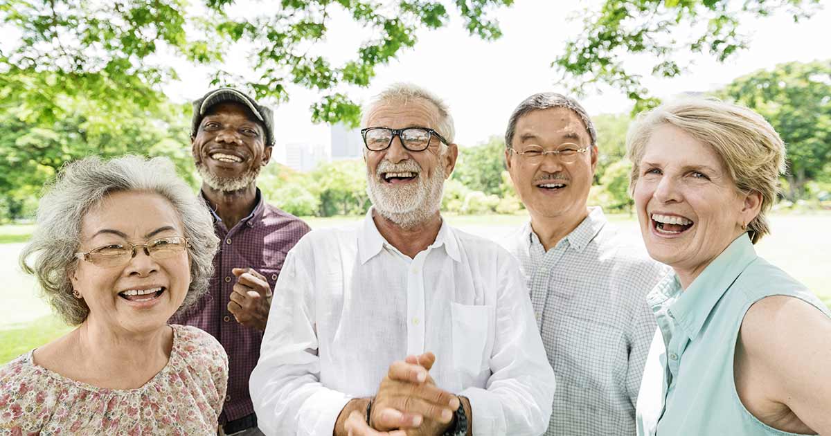 A group of five older people laughing and smiling together in a park