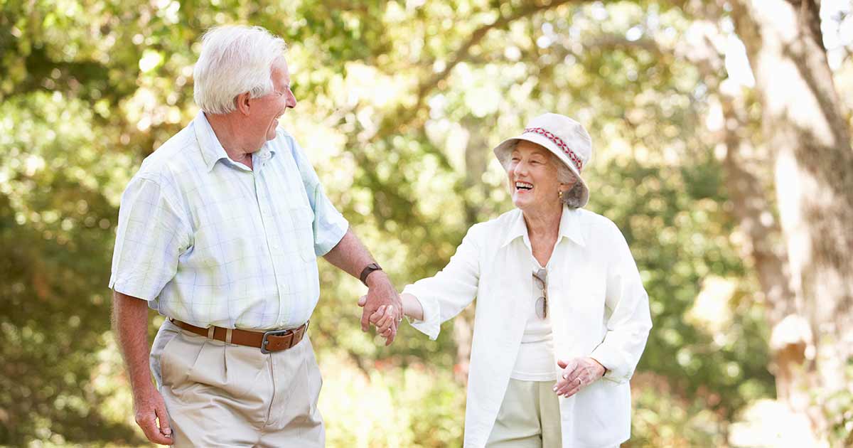 An older couple laughing and walking through a park