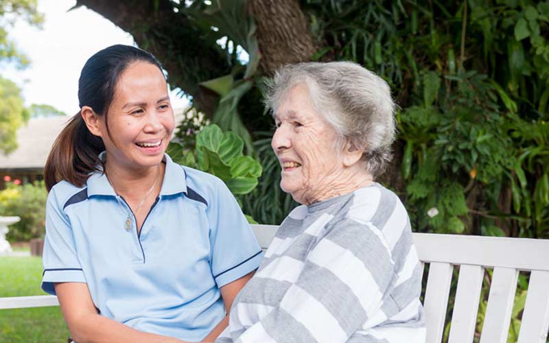 Blue Care staff member sitting with client in garden smiling at each other.