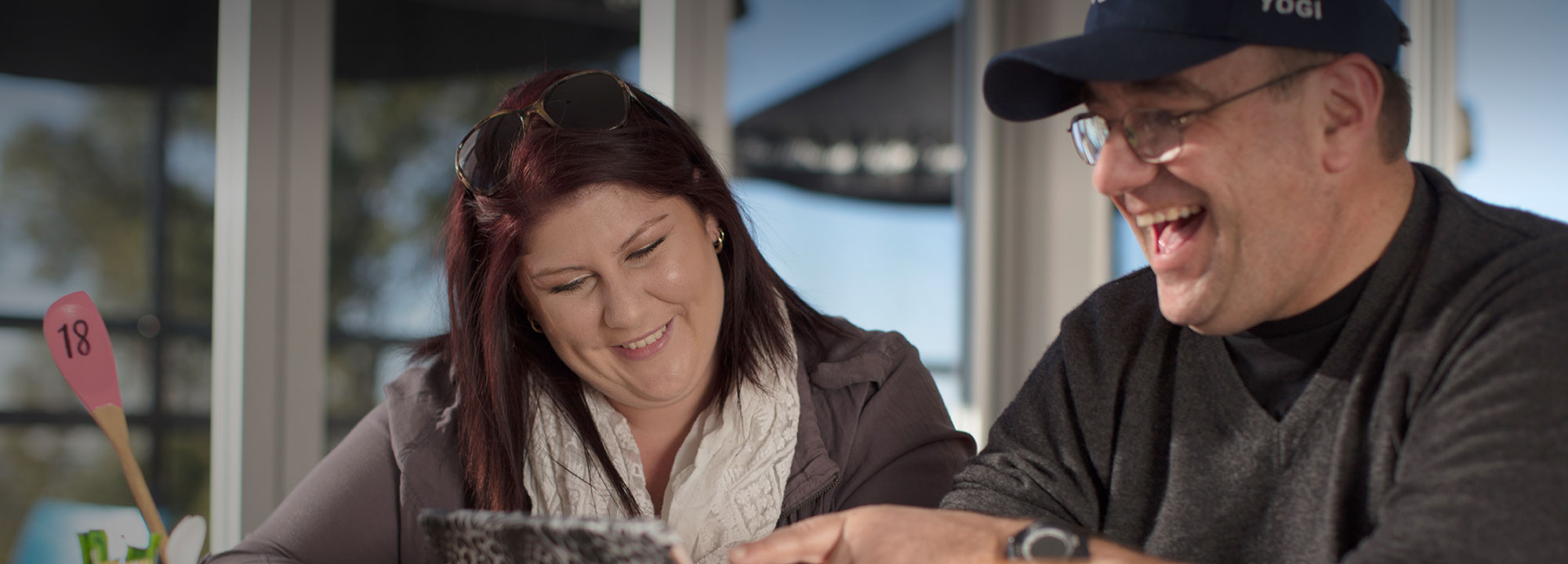man and woman sitting outside smiling and looking towards a laptop screen