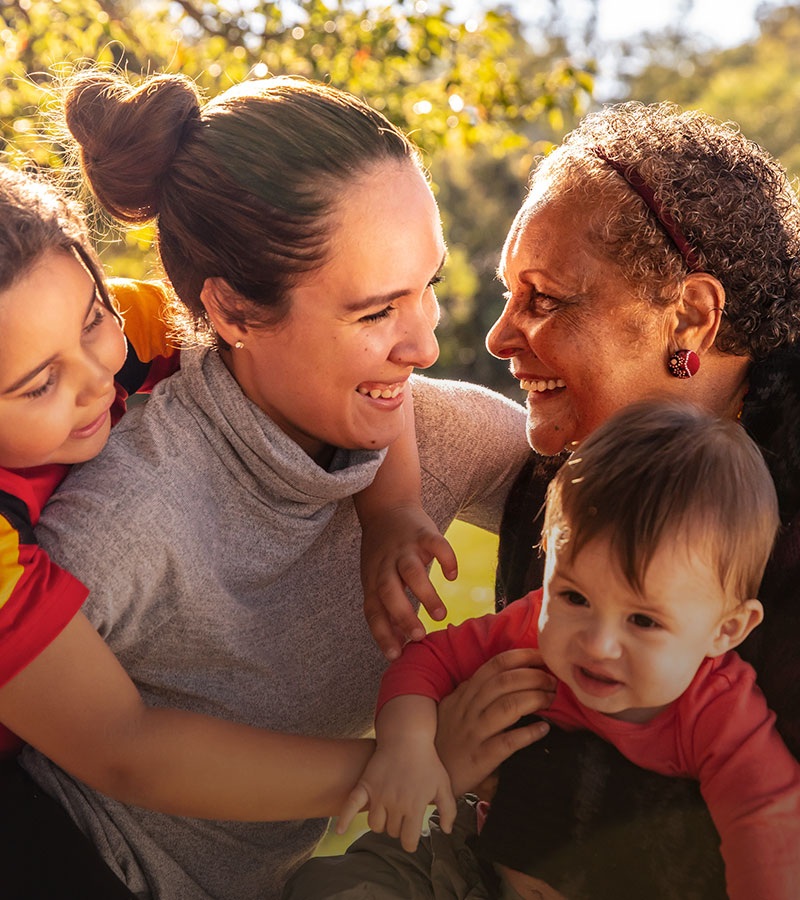A smiling older lady and younger woman play with two children in a park.