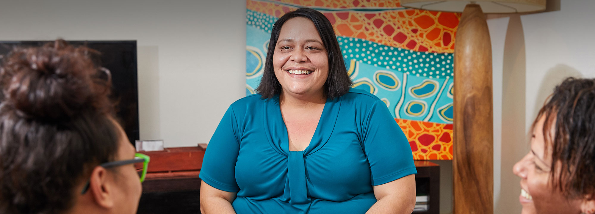 an indigenous lady sitting indoors in front of indigenous artwork