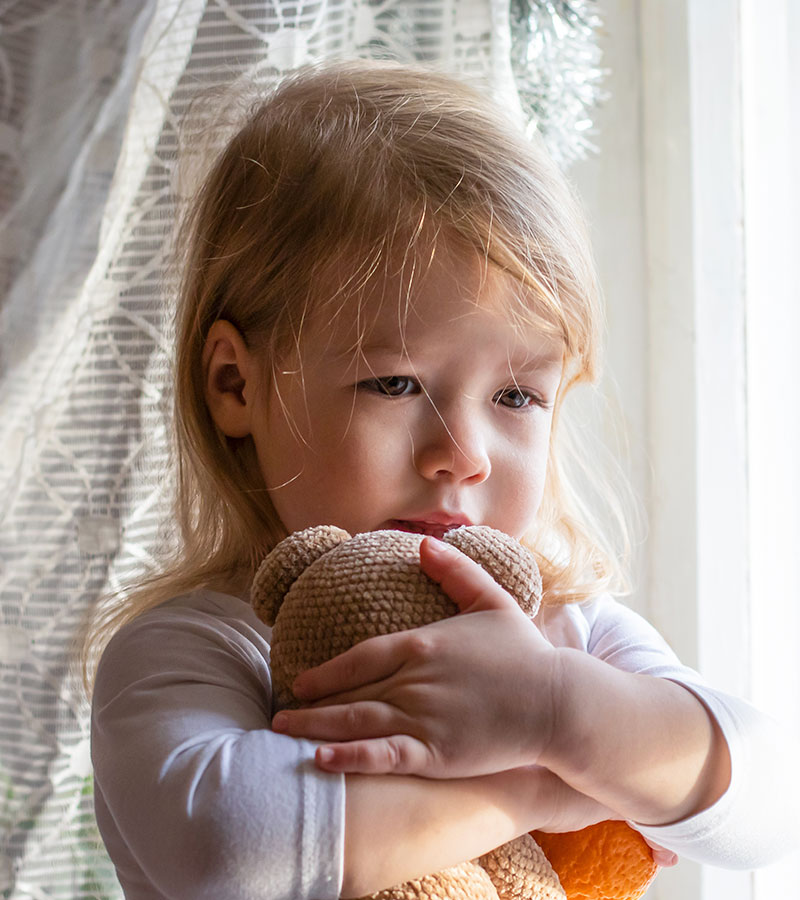 A young girl hugging a plush toy teddy, looking concerned in deep thought