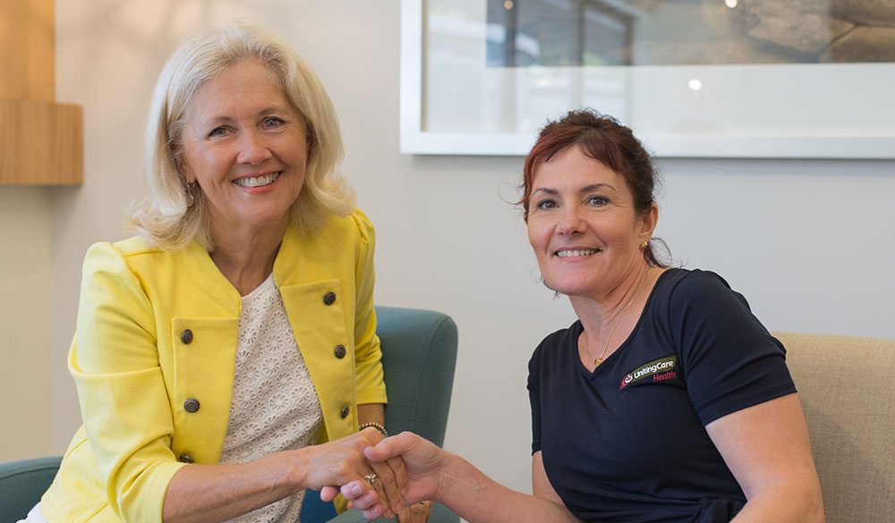 female staff member shaking hands while smiling indoors with an elderly female client