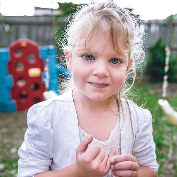 young blonde-haired girl standing outdoors smiling into the camera