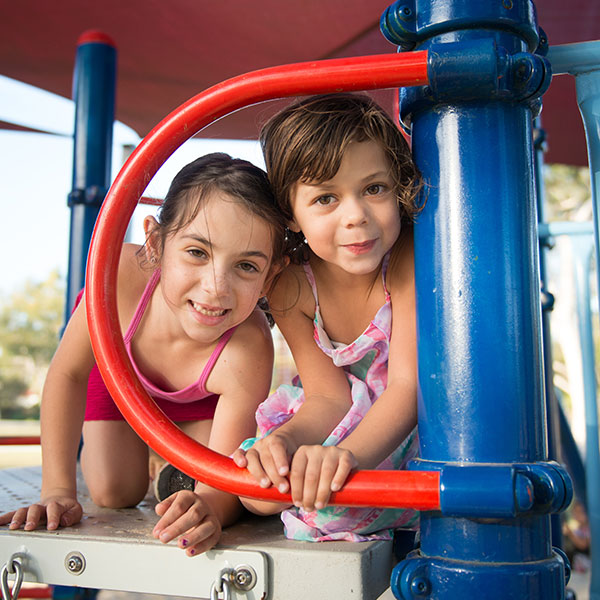 two young girls crawling in a playground smiling into the camera