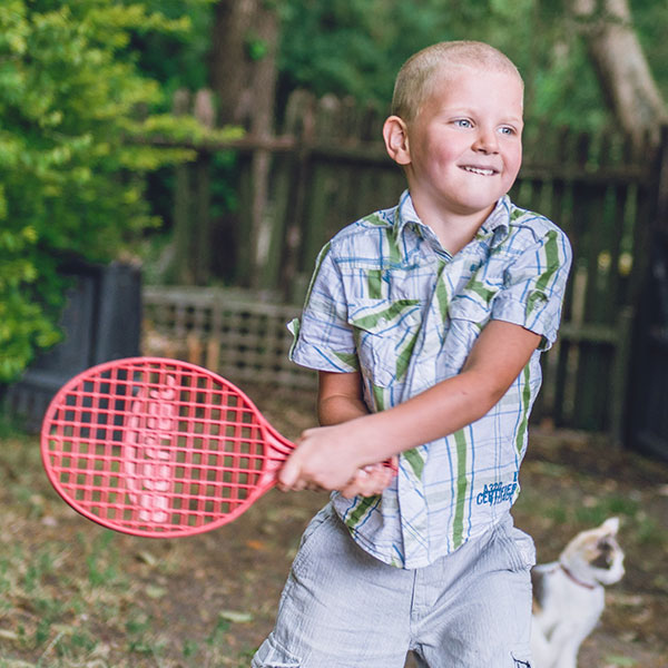 young boy playing tennis outdoors about to swing his racquet