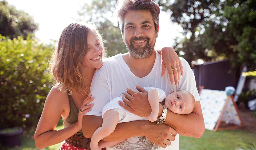 man and women embracing with an infant child laying in the man's arms