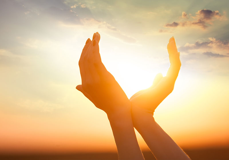 two hands cupping the sunlight as it radiates from a vibrant sunset taking place in the background