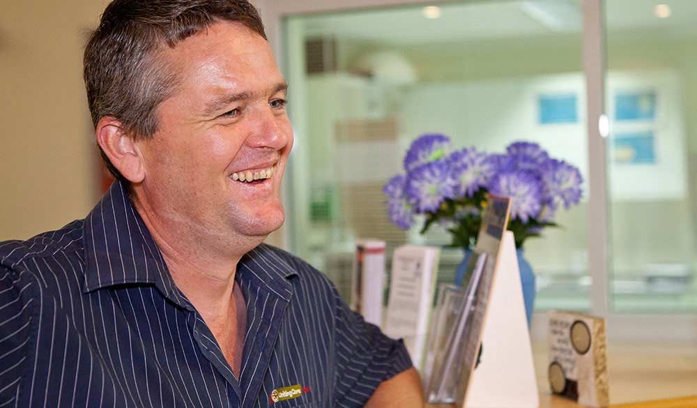middle aged man with black hair smiling towards someone out of frame inside a hospital building