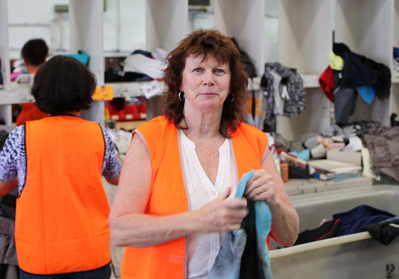 female volunteer wearing a bright orange vest working in a clothing donation facility