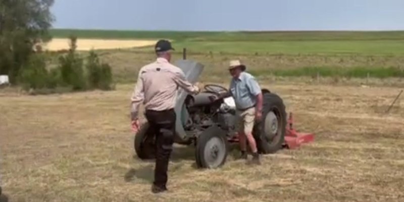 Farmer crisis supporter, Ken, is reaching out to shake hands and have a chat with a farmer working on his tractor
