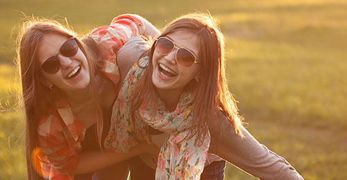 two young women with sunglasses with arms around each other smiling to the camera