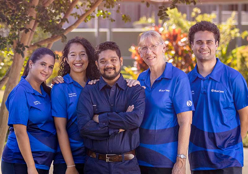 Five BlueCare workers in uniform stand in a garden near a driveway.