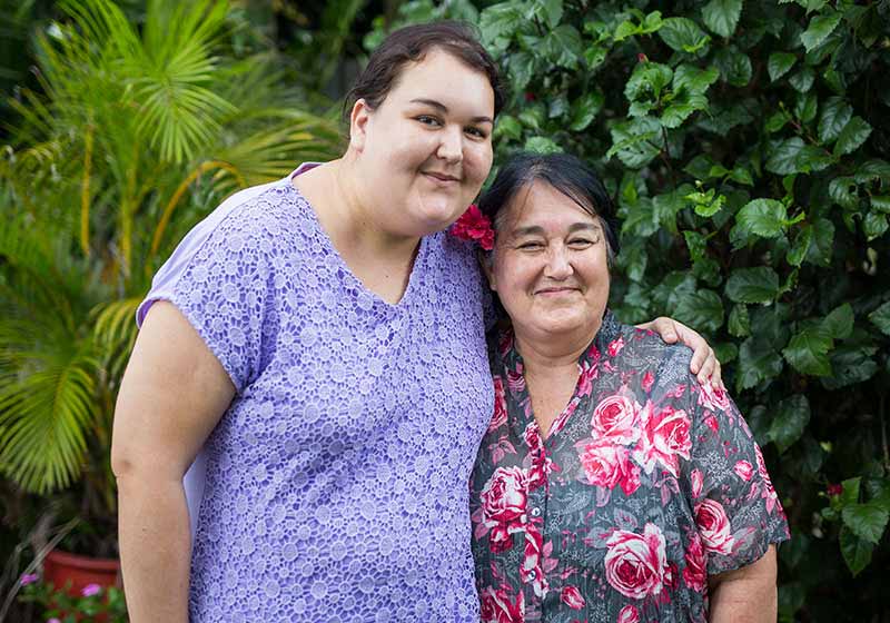 two woman smiling outdoors with their arms around one another