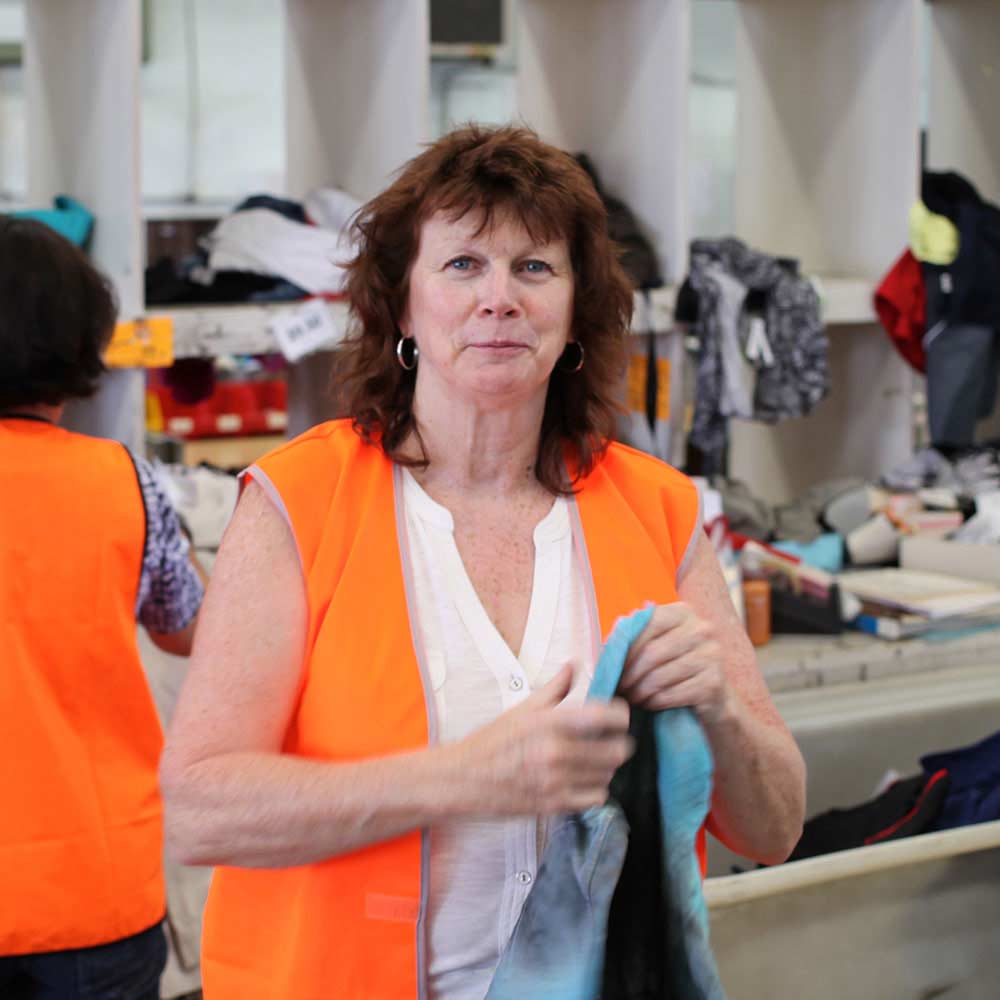 female volunteer wearing a bright orange vest working in a clothing donation facility