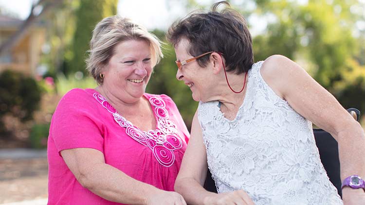 elderly lady sitting outdoors smiling next to a volunteer