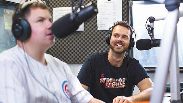 two young men sitting in a radio studio with microphones in front of them