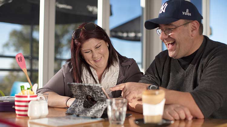 man and women sitting outdoors smiling while watching ipad