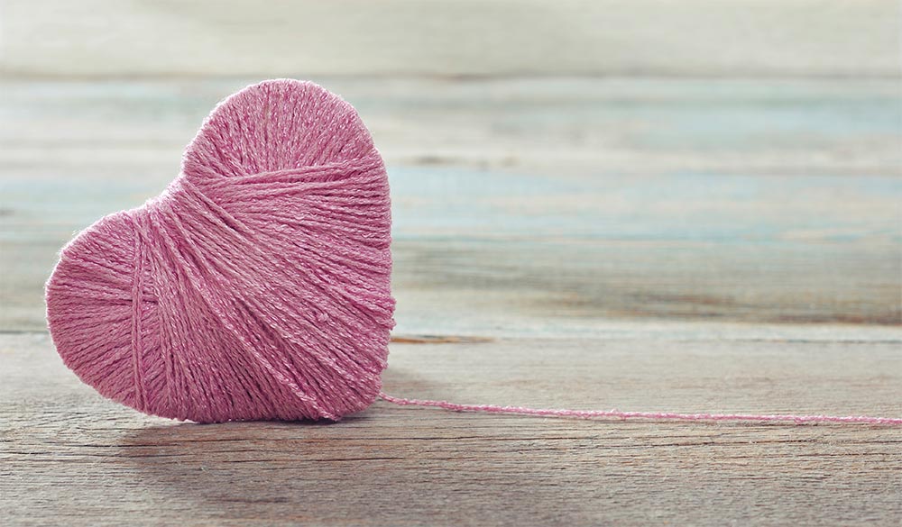 love heart made of yarn sitting on wooden bench