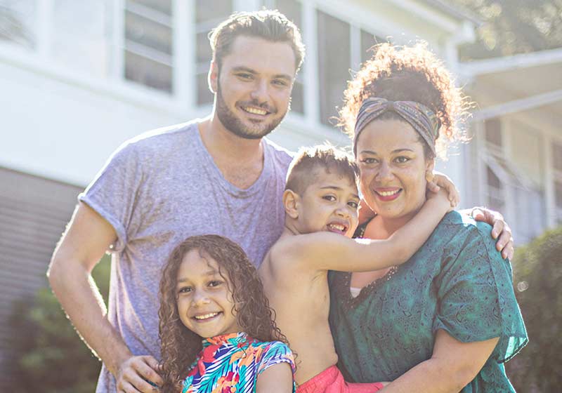 mother and father with their young children standing out the front of a house smiling