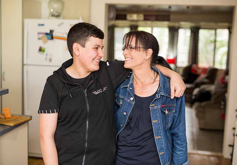 mother and her teenage son indoors hugging and smiling