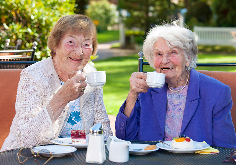 elderly women smiling have tea outside