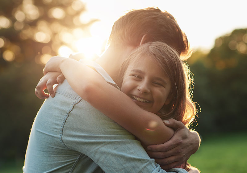 father and daughter hugging in a park at sunset