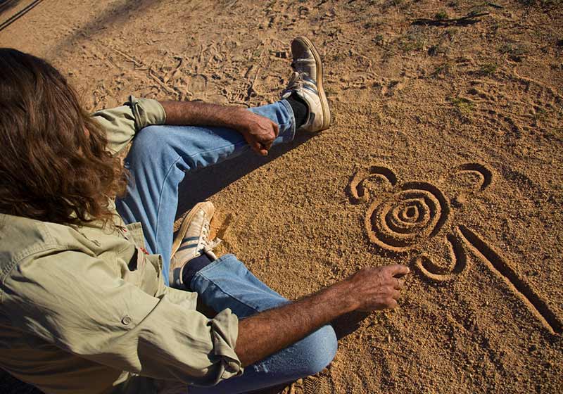 man sitting on the sand drawing a symbol