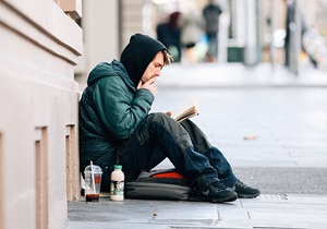 homeless man sitting on city street smoking and reading