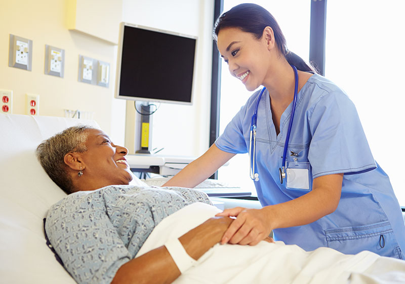smiling older woman laying in hospital bed while happy female doctor tends to her