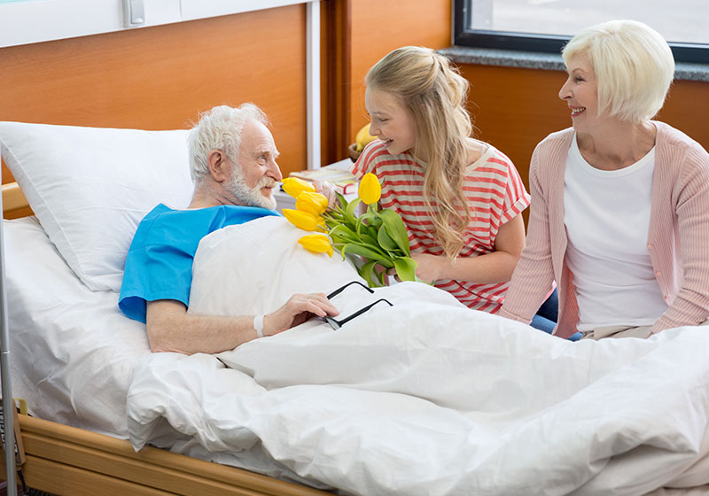 granddaughter gives flowers to sick grandfather in hospital bed