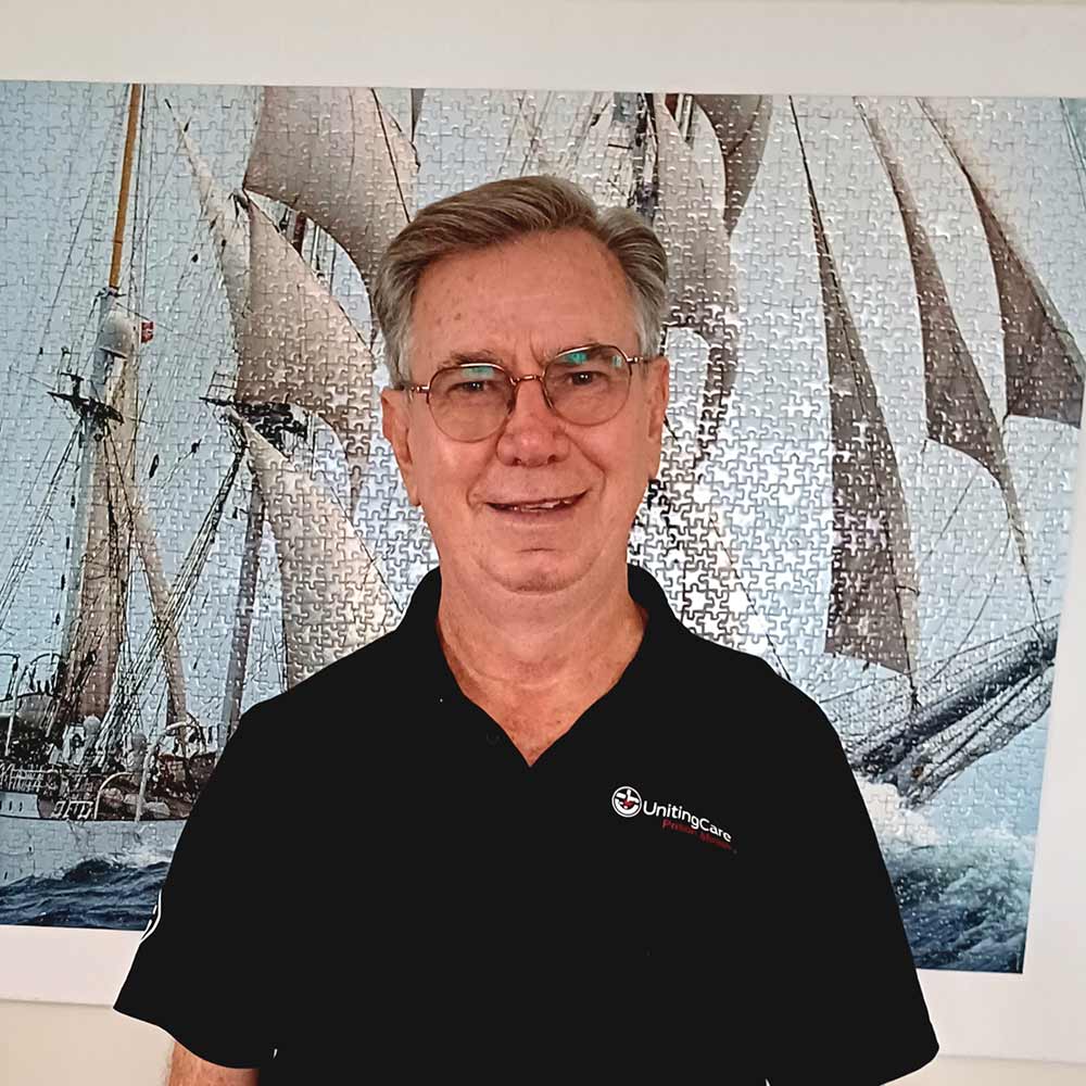 UnitingCare Prison Chaplain Ray Scarlett stands in front of an image of a tall ship.