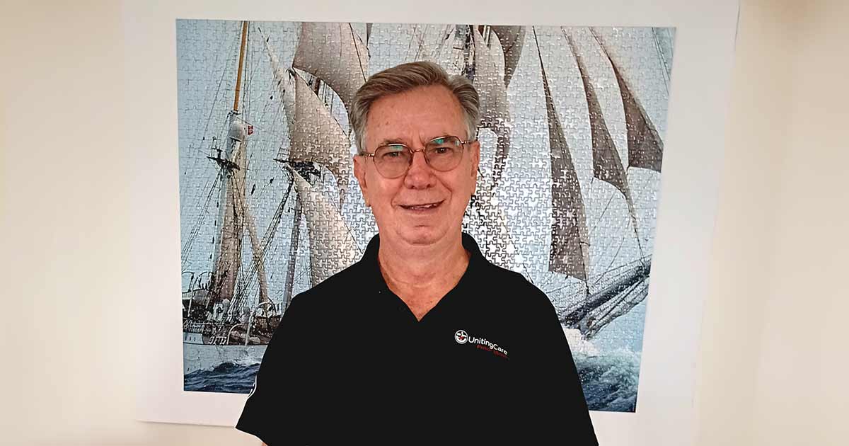 UnitingCare Prison Chaplain Ray Scarlett stands in front of an image of a tall ship.