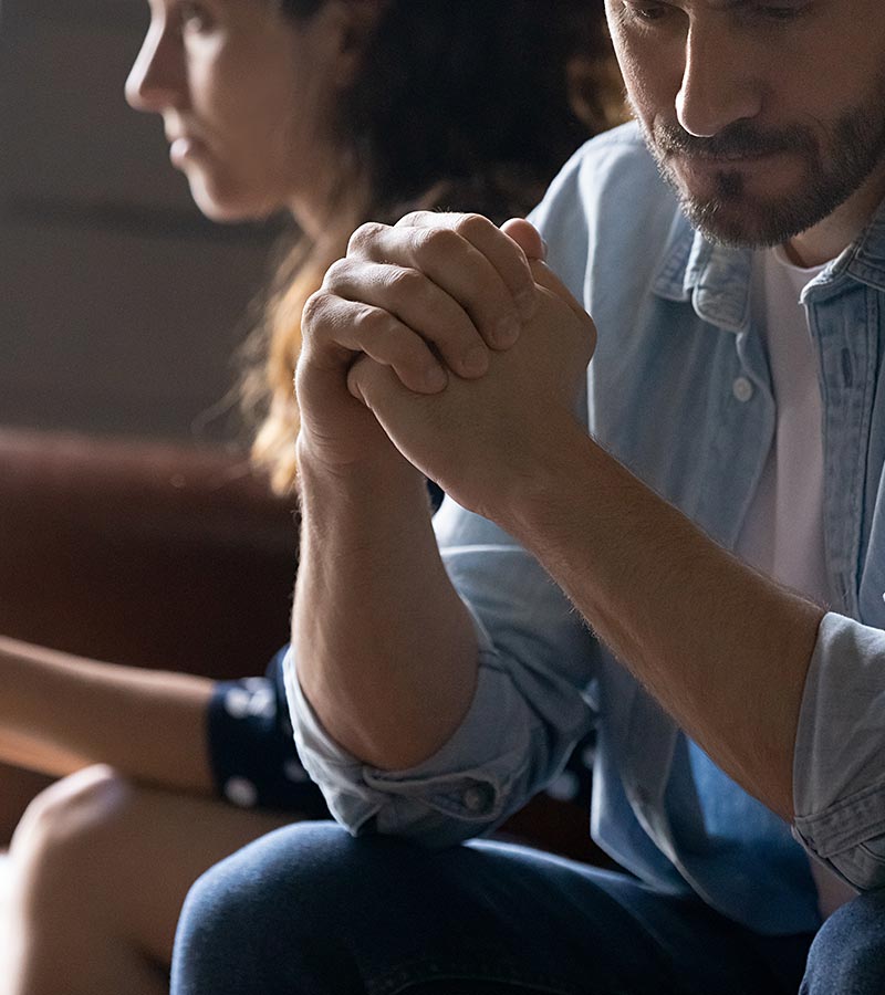 An unhappy couple sit together on a couch