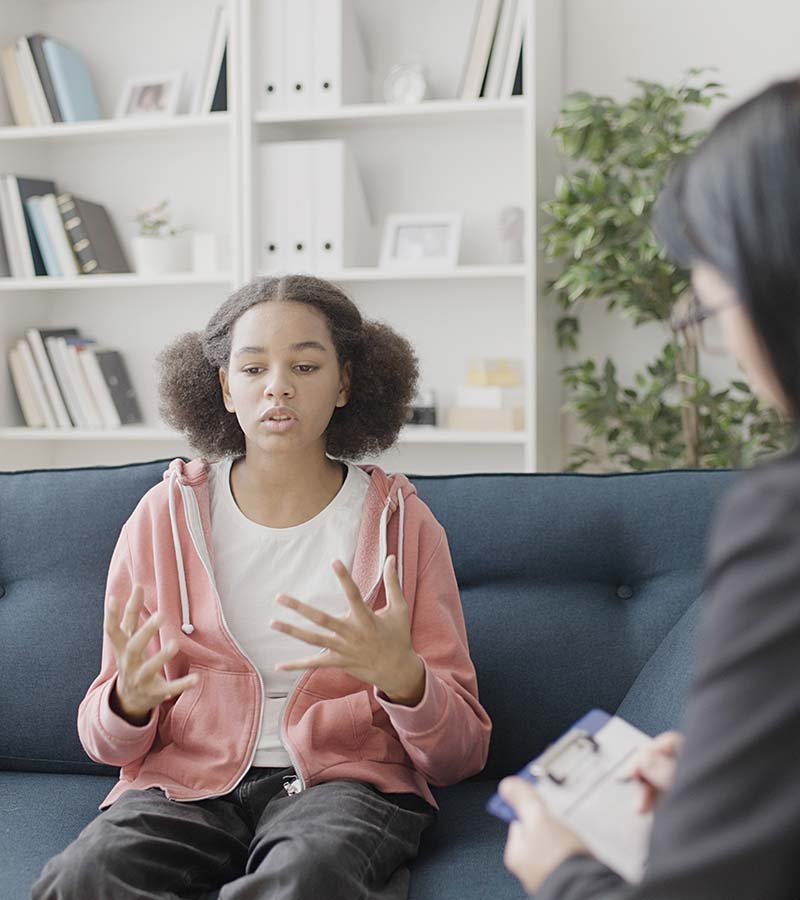 A young girl sits on a couch, talking to a counsellor.