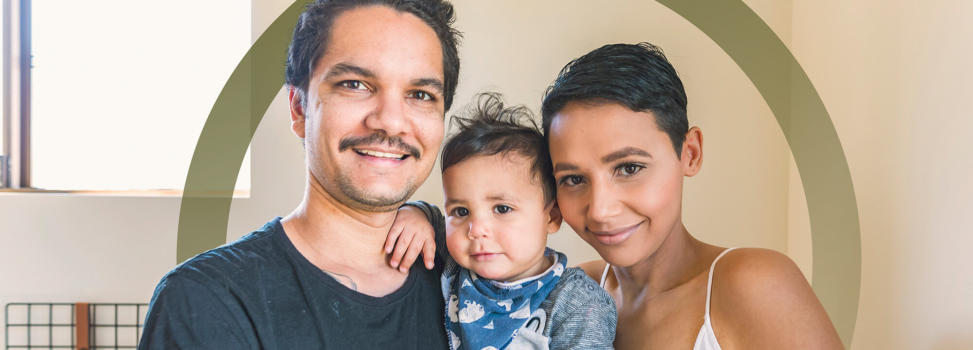 Happy young Aboriginal mum and dad hold their baby between them.