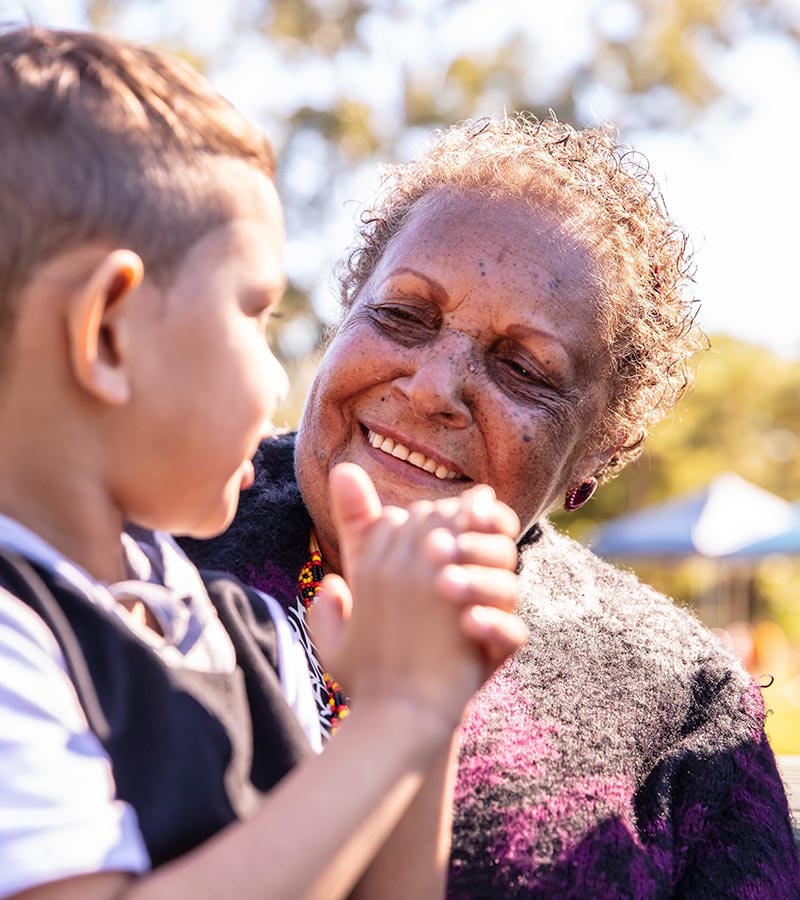 A lady in a park smiling at a younger boy