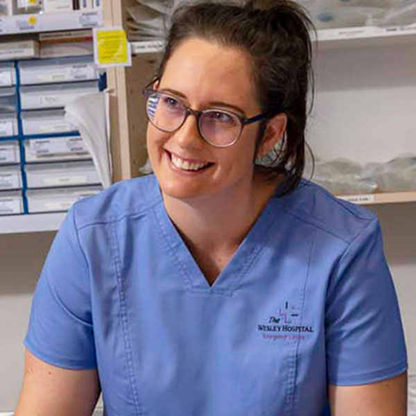 A young Wesley Hospital graduate nurse program participant smiles as she assists a patient in a hospital bed.