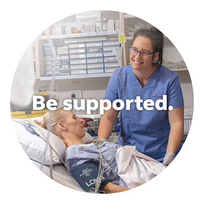 A smiling young graduate nurse talks to patient lying in a hospital bed.