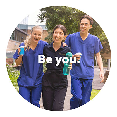 Three young graduate nurses in hospital uniforms laugh as they stroll the hospital grounds.